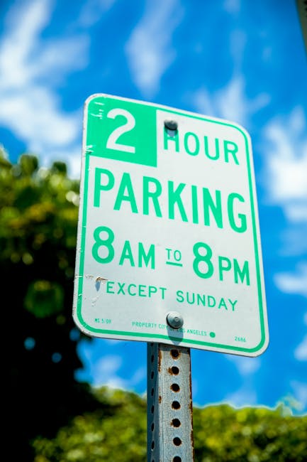 A rectangular white sign with bold black lettering stating 'NO PARKING DAY OR NIGHT' is mounted on a grey wooden door or panel, secured with four screws, two in the top corners and two in the bottom corners. The background consists of horizontal and vertical grey wooden planks, possibly part of a garage or building exterior. The lighting is neutral, indicating an outdoor setting. This sign is relevant to house removals and furniture transport, as it indicates parking restrictions that may affect loading and unloading processes during home relocation, which is a key consideration in planning moves according to Islington Council parking permit rules for removals, as explained by Islington Movers.